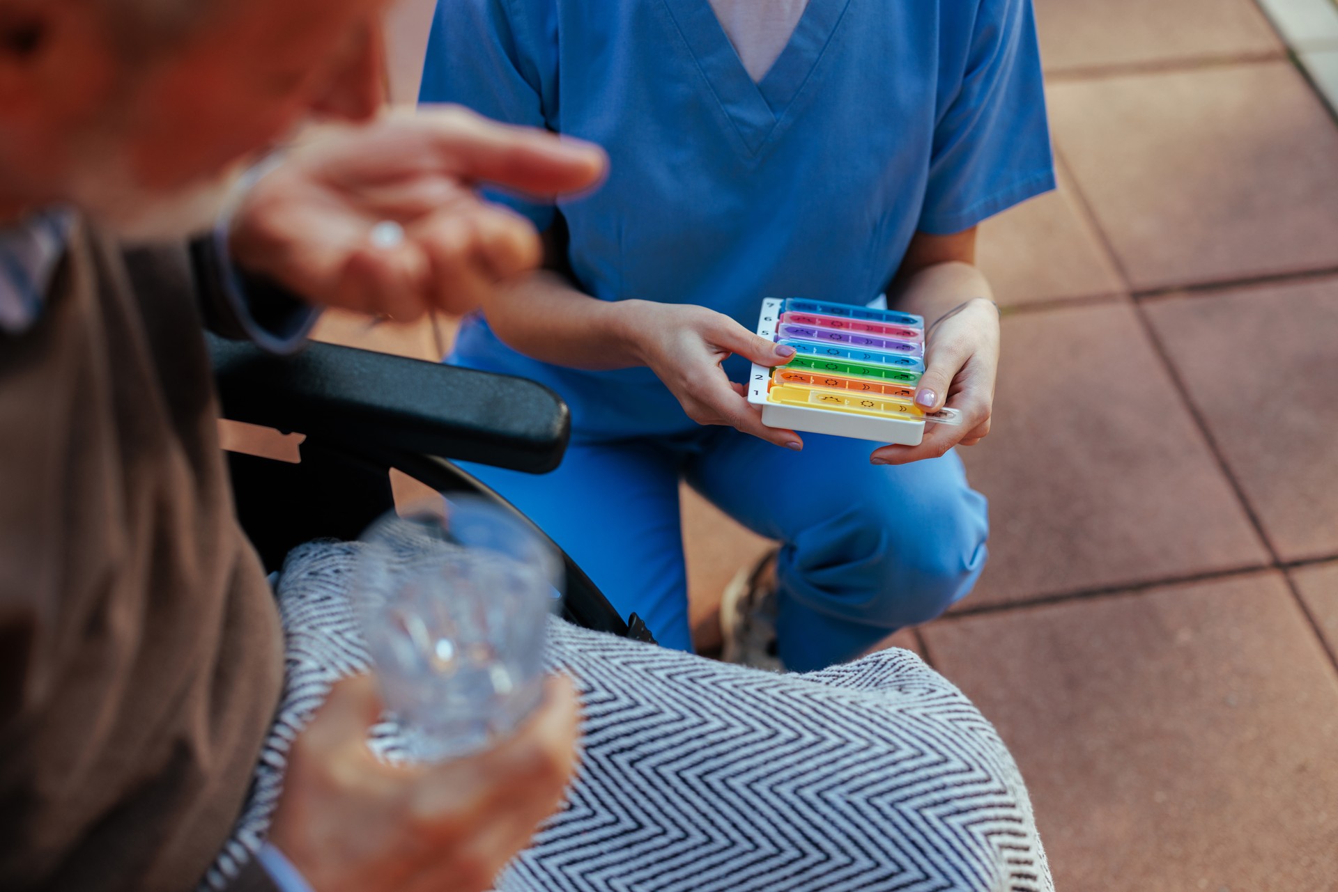 Caregiver with a pillbox assisting elderly man in nursing home.